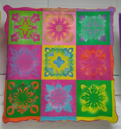 Appliqued quilt made 3 by 3 grid of squares in bright neon colours depicting flowers