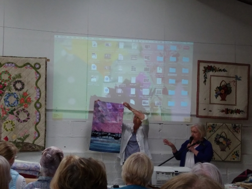Person holding up artwork while second person talks to group of people with a microphone