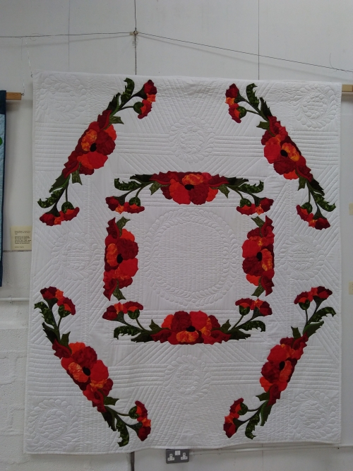 Poppy Wreath by Kathleen Hughes: White rectangular quilt decorated with quilted poppies