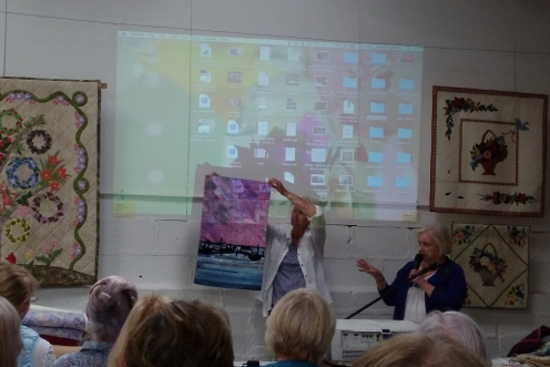Person holding up artwork while second person talks to group of people with a microphone