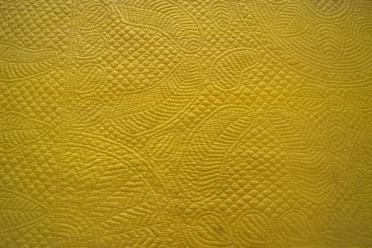 Yellow quilt with stitched patterns of leaves, fans.