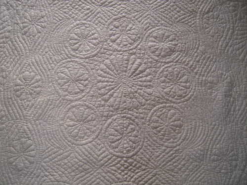 Close up of an embroidered pattern on an off white quilt