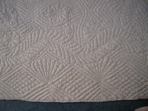 Close up of an embroidered pattern on an off white quilt
