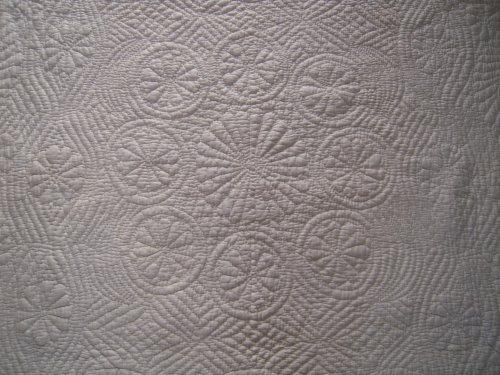 Close up of an embroidered pattern on an off white quilt