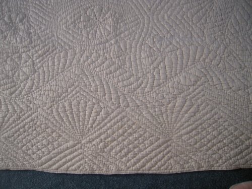 Close up of an embroidered pattern on an off white quilt