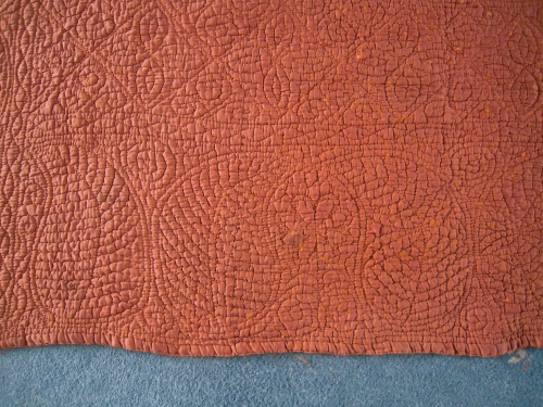 Close up of border of rust coloured welsh quilt showing large curved Paisley pears stitching