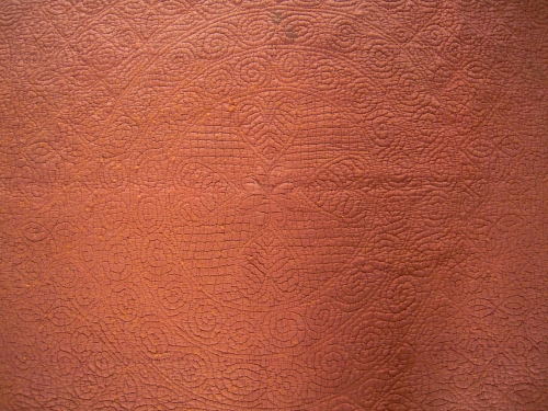 Close up of central wheel stitching pattern of rust coloured welsh quilt