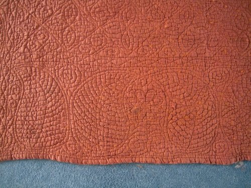 Close up of border of rust coloured welsh quilt showing large curved Paisley pears stitching