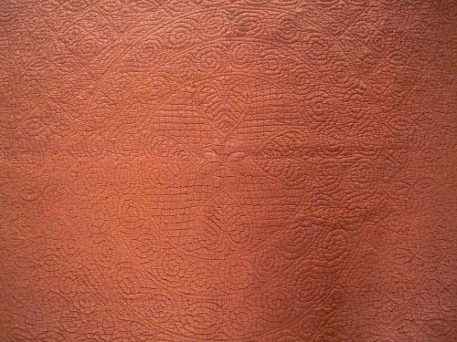 Close up of central wheel stitching pattern of rust coloured welsh quilt