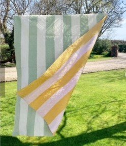 Green and cream strippy quilt with reverse of yellow and pink strips hanging on line