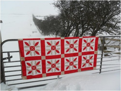 Red and white quilt hanging over fence in snow