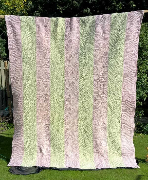 Pink and cream strippy quilt hanging in garden