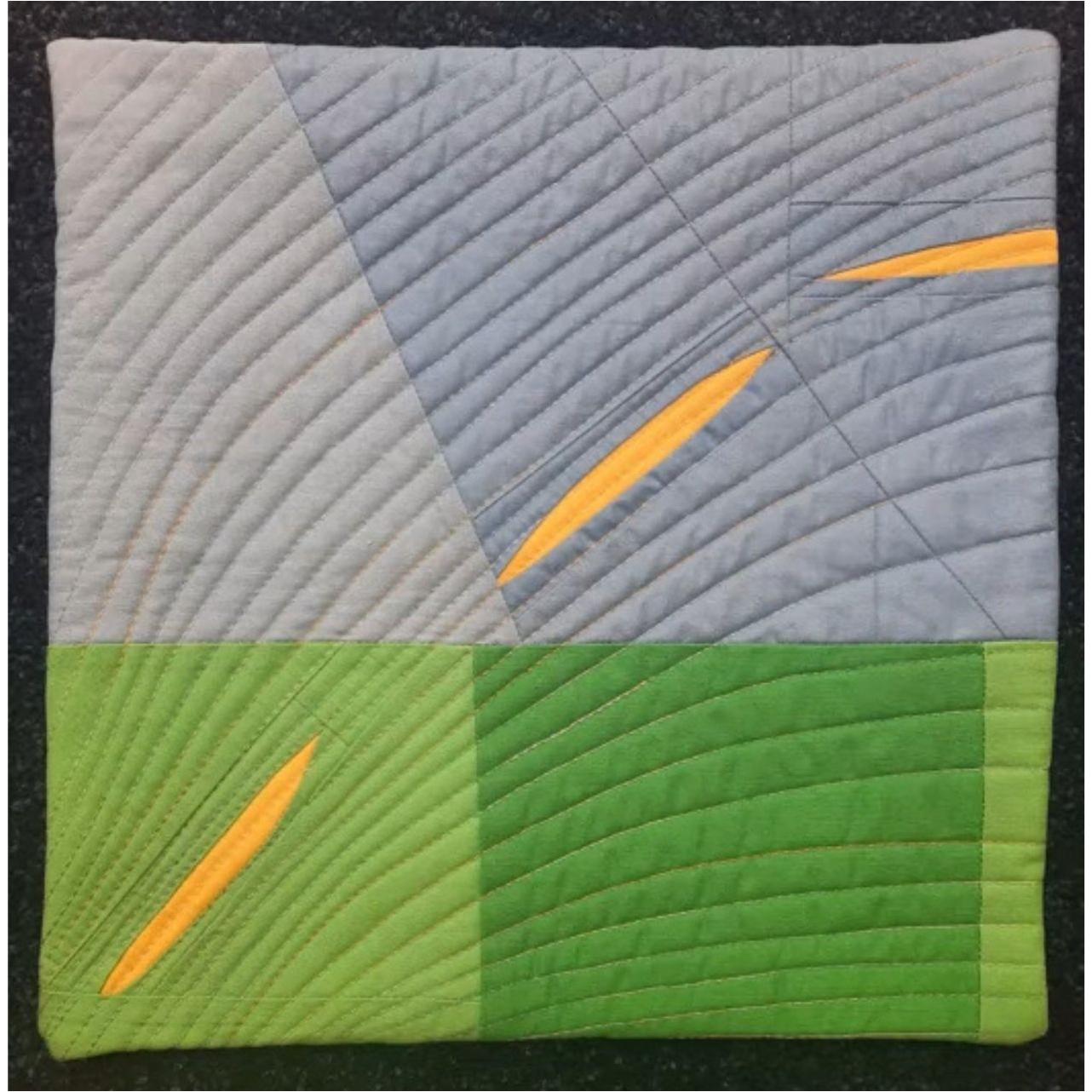 A square quilt with a gray and green background. The quilt features a geometric design with curved lines and yellow shapes, resembling leaves or petals. The background is quilted with a curved linear pattern.