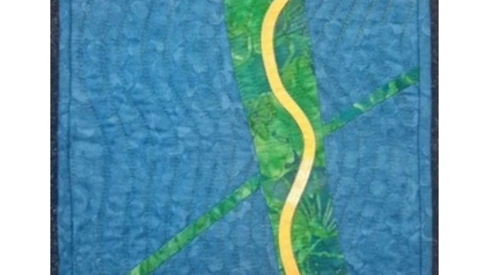  A square quilt with a blue background and a yellow, winding path. The path is surrounded by green fabric with a textured pattern, resembling a forest or jungle. The quilt has a simple, minimalist design with a focus on the contrasting colors and textures.