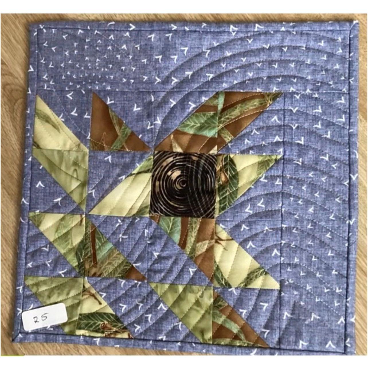 A square quilt with a blue background. The quilt features a central star design made up of triangles in shades of brown and green. The background is filled with a pattern of small, white triangles. 