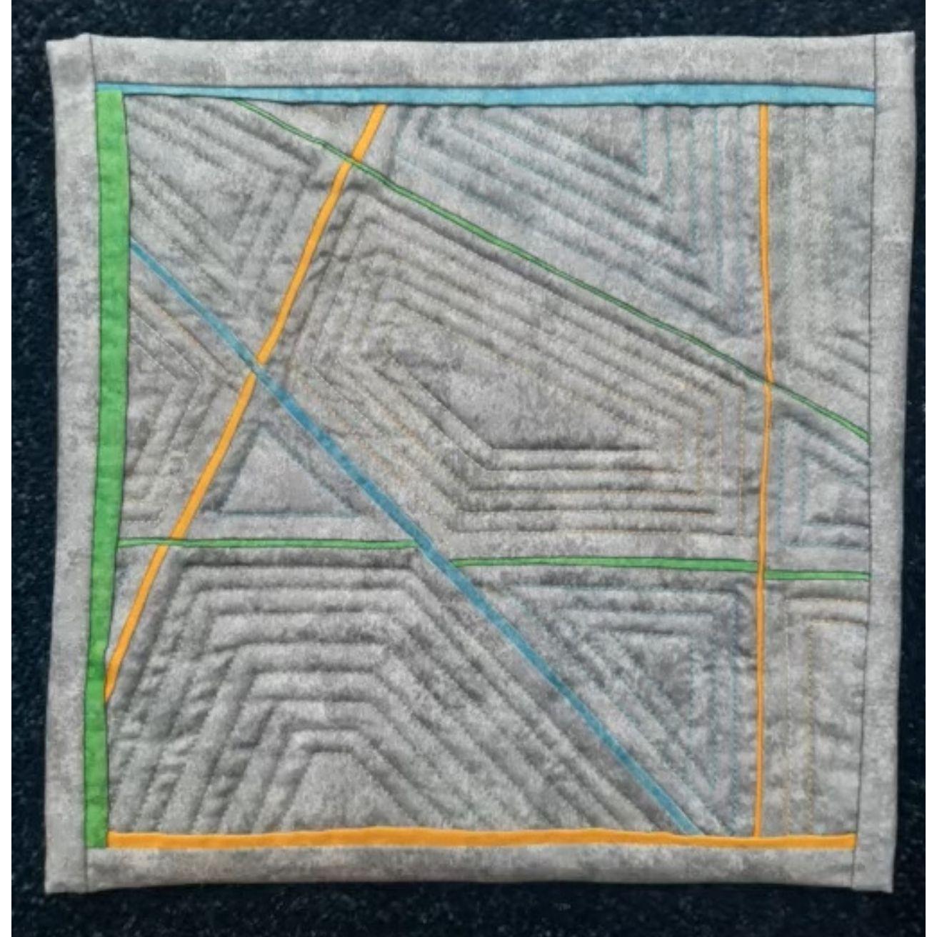 A square quilt with a gray background and a colorful border. The quilt features a geometric design with intersecting lines in yellow, green, and blue. The background is quilted with a linear pattern.