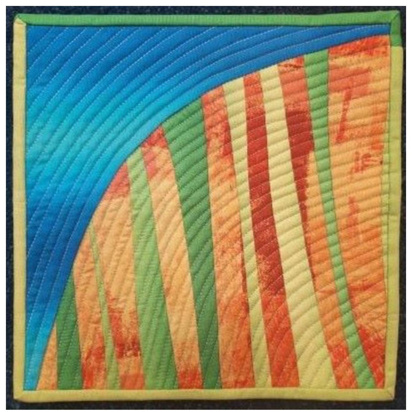 A colourful quilt with a landscape-like design. The quilt features a curved blue section representing the sky, transitioning into vertical strips of green, yellow, and orange, resembling fields or hills. The fabric has a textured, almost painted look, with visible stitching lines adding depth.