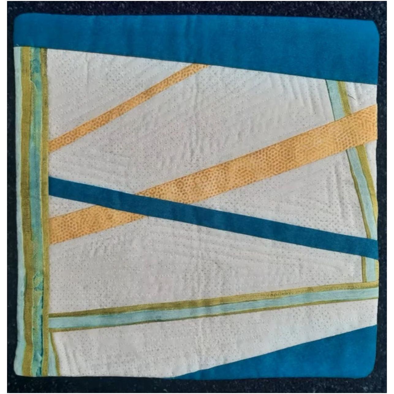 A square quilt with a blue background. The quilt features a colorful, abstract design with intersecting lines in shades of orange, yellow, and blue. The background is quilted with a linear pattern.