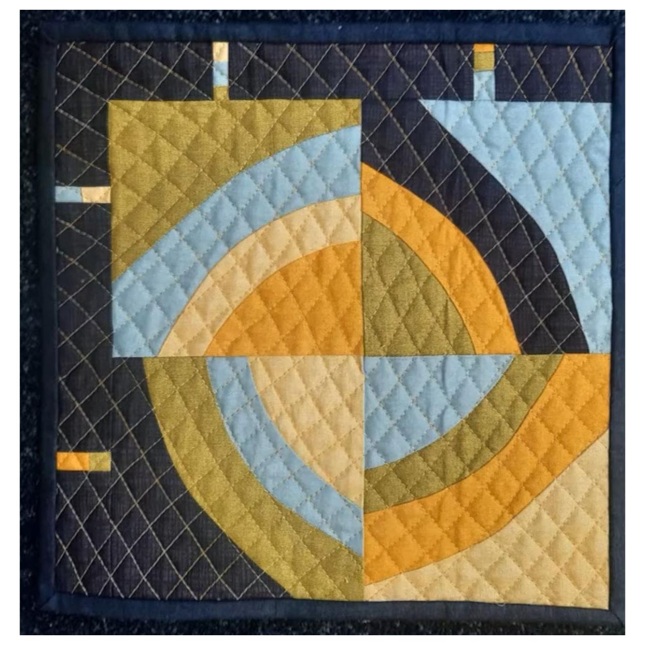 A square quilt with a dark blue background and a colorful, geometric design. The quilt features curved shapes in shades of blue, green, and yellow, arranged in a circular pattern. There are also thin, vertical lines in the corners. The background is quilted with a diamond pattern.