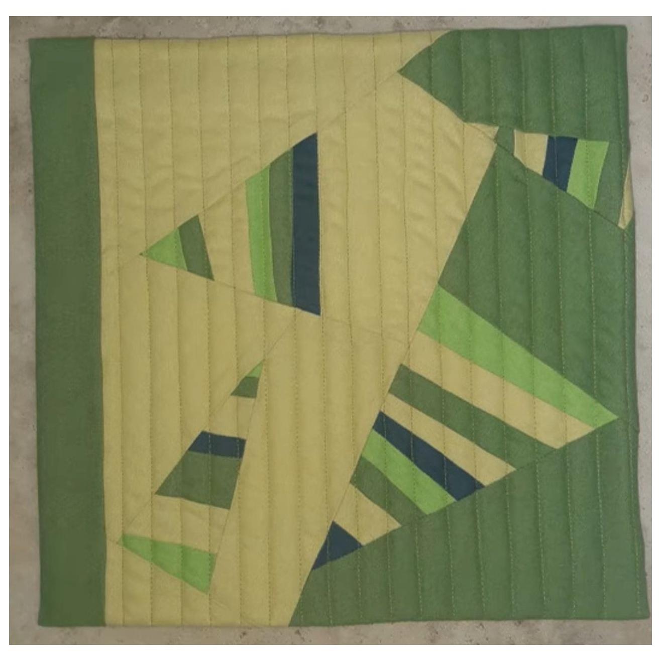 A square quilt with a green background. The quilt features a geometric design with triangles in shades of green and blue. The triangles overlap and create a sense of depth and dimension. The background is quilted with vertical lines.