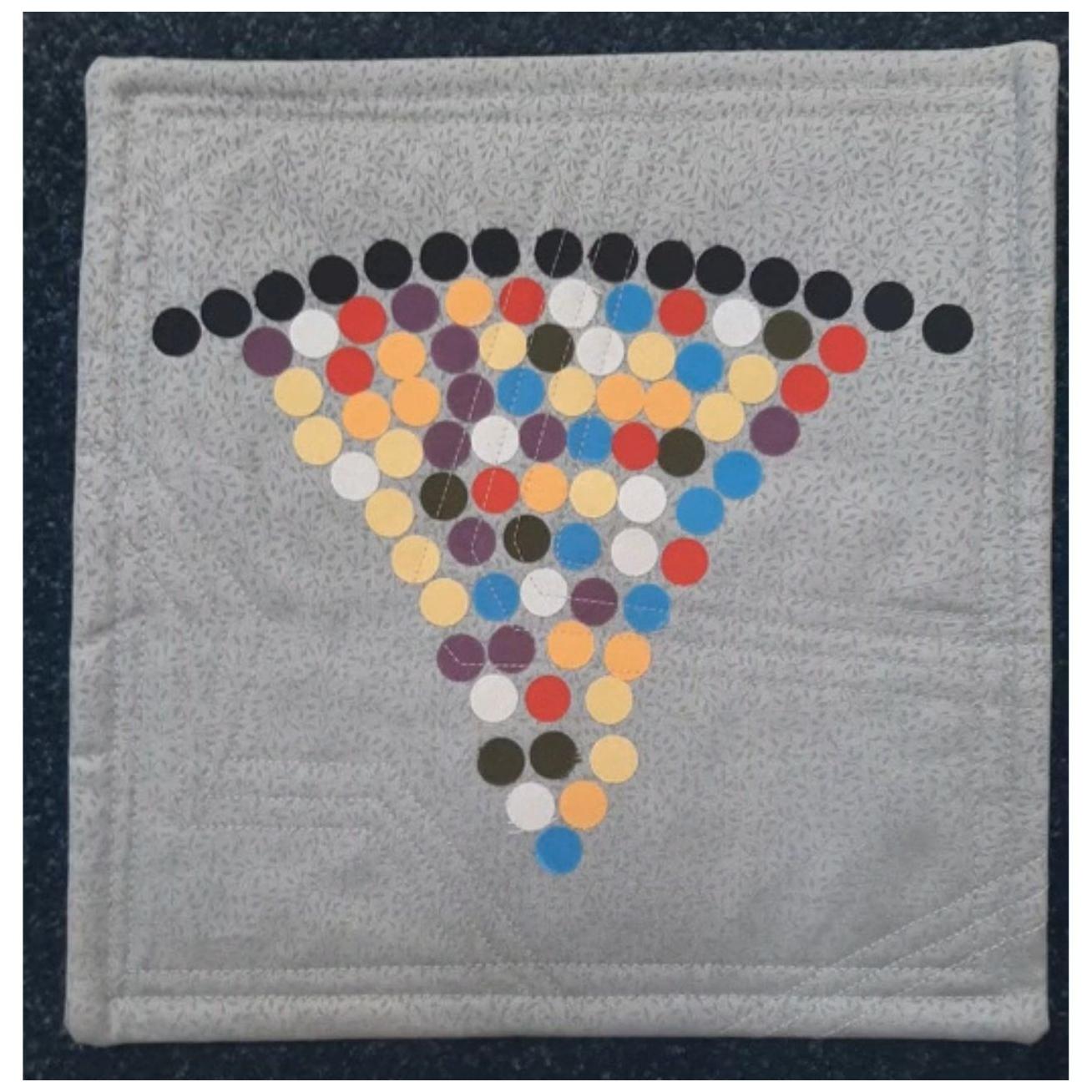 A square quilt with a gray background. The quilt features a colorful, geometric design with circles arranged in a triangular pattern. The circles are in various colours, including red, orange, yellow, green, blue, and purple.