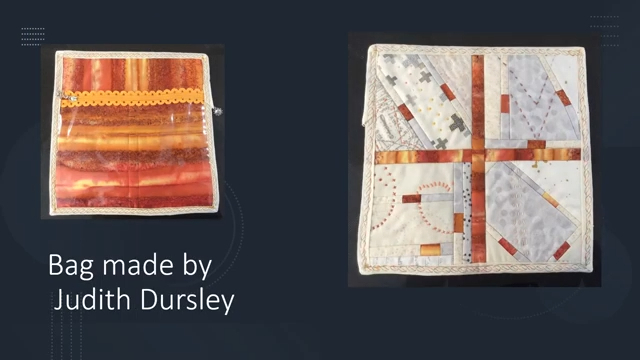 A rectangular bag with a zipper and a clear plastic pocket. The bag inside features a colourful, abstract design with stripes in shades of orange and red. The outside of the bag features a geometric pattern in white, grey, orange and red.