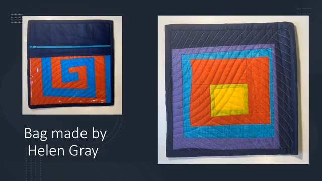 A square quilted bag with a dark blue background and a colourful, geometric design of nested square pattern in blue, purple, orange, yellow, and green. The inside of the bag features a pieced rectangular swirl and a bright blue zipper.