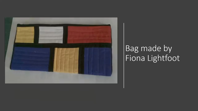 A rectangular bag with a geometric pattern in red, yellow, blue, white, and black. The bag has a quilted texture.