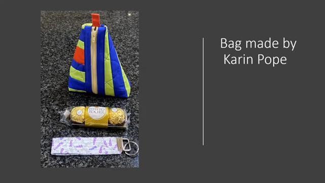 A triangular-shaped bag with a zipper closure. The bag is in blue and yellow with a red accent. Next to it are a box of chocolates and a purple key chain.