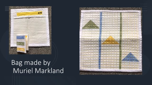 A square bag with a zipper and a clear plastic pocket. The front of the bag has a geometric design featuring triangles in blue, yellow, and green. The bag has been quilted with a grid pattern.