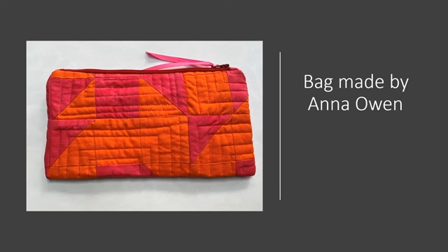 A pink, quilted zipper pouch. The pouch has a geometric pattern with triangles and rectangles. There is a pink ribbon attached to the zipper.