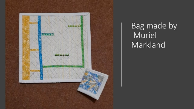 A square, quilted bag. The bag has a colourful patchwork design with geometric shapes. Next to the bag is a small, rectangular piece of fabric with an abstract pattern.