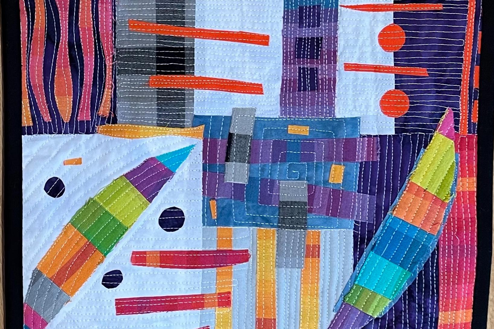 A colourful, abstract quilted bag front with a predominantly white background. The quilt features various geometric shapes, including rectangles, triangles, and circles, in a vibrant array of colours such as red, orange, yellow, green, blue, and purple. T