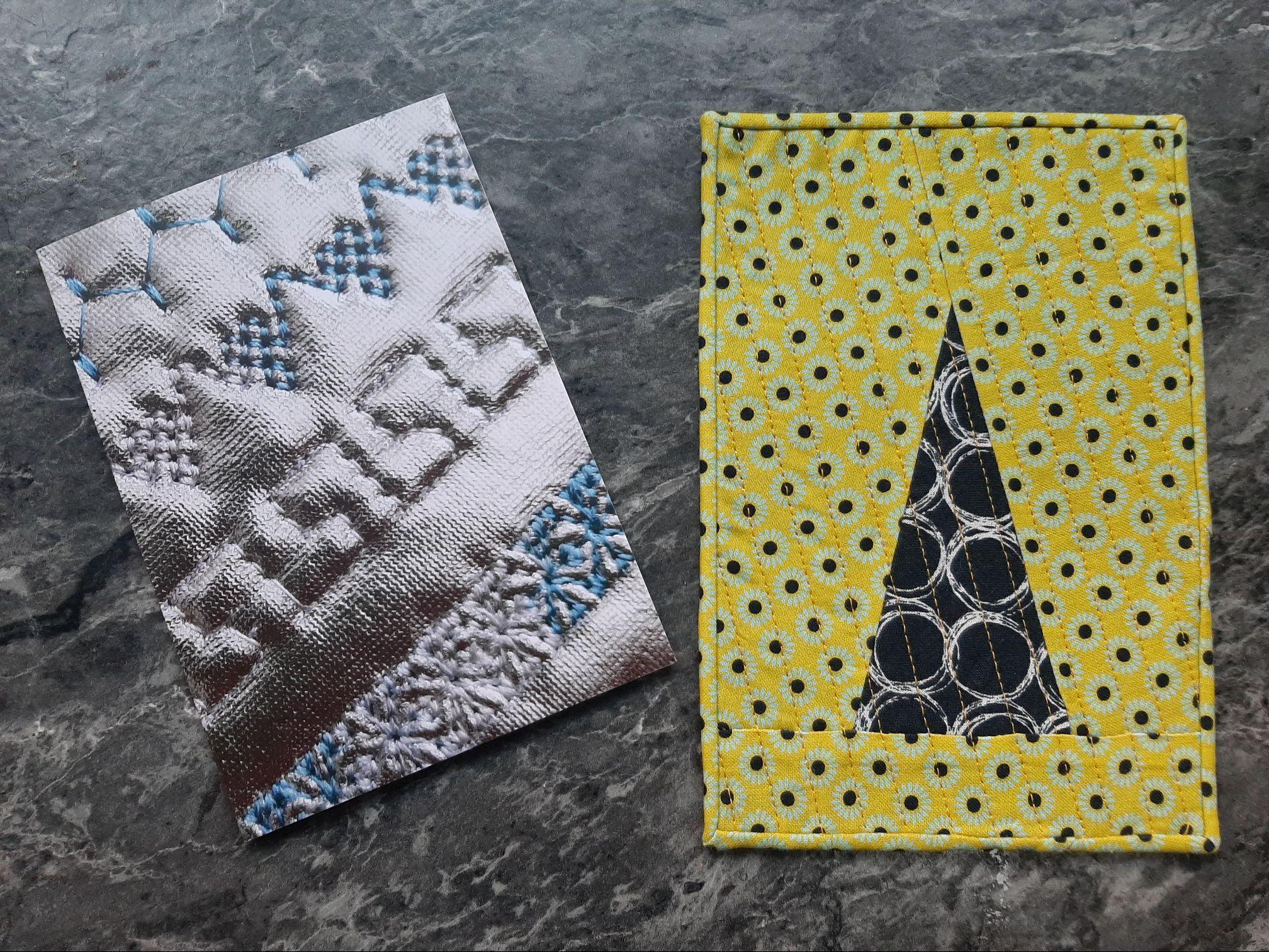 A rectangular quilt with a white background. The word "PEACE" is embroidered in blue thread in a stylised font. The background is quilted with a textured, linear pattern. A rectangular quilt with a yellow background. The quilt features a black triangle shape with a circular pattern inside. The background is filled with small, white flowers.