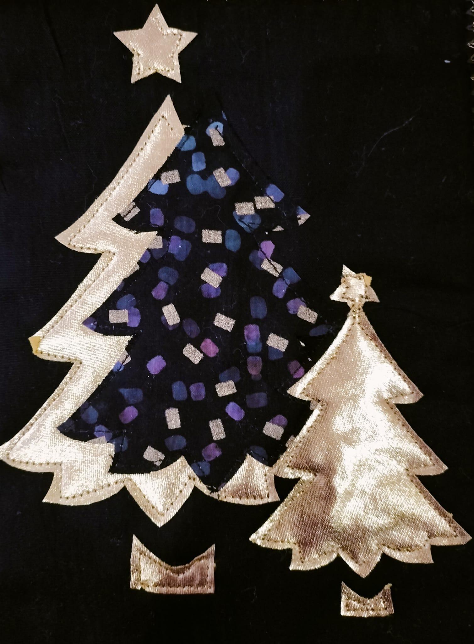 A square quilt with a black background. The quilt features three Christmas trees of different sizes. The largest tree is decorated with a star and has a colourful, patterned design. The other two trees are gold. The background is quilted with a linear pattern.