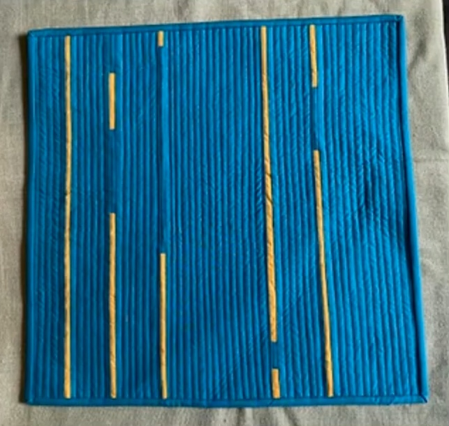 A rectangular quilt with a blue background. The quilt features vertical, yellow lines of varying lengths. The background is quilted with a subtle, linear pattern.