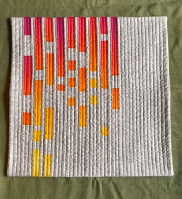 A square quilt with a white background. The quilt features a colorful, geometric design with vertical lines in shades of red, orange, and yellow. The lines are arranged in a staggered pattern, creating a sense of movement and rhythm. The background is quilted with a linear pattern.