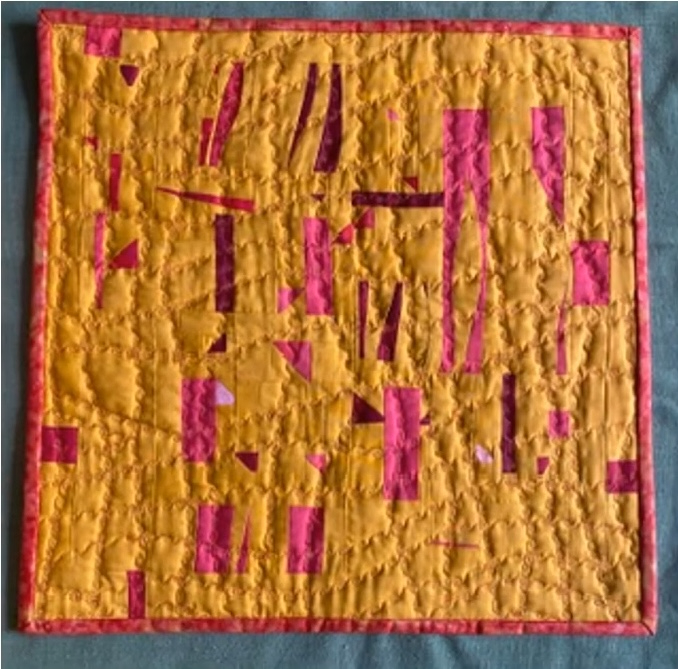 A square quilt with a yellow background. The quilt features a geometric design with overlapping shapes in pink and red. The background is quilted with a wavy pattern. The quilt has a red border.