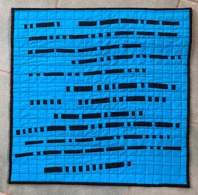 A square quilt with a blue background. The quilt features a pattern of black lines of varying lengths, arranged in a seemingly random pattern. The background is quilted with a grid-like pattern.