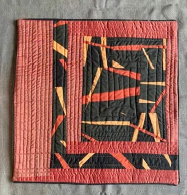 A square quilt with a predominantly red background. The quilt features a geometric design with black and orange shapes, creating a sense of depth and dimension. The background is quilted with a linear pattern. 