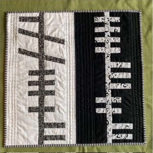 A square quilt with a black and white color scheme. The quilt is divided into two sections: the left side has a white background with black vertical lines, and the right side has a black background with white vertical lines. The lines have a textured pattern. The quilt has a black and white striped border.