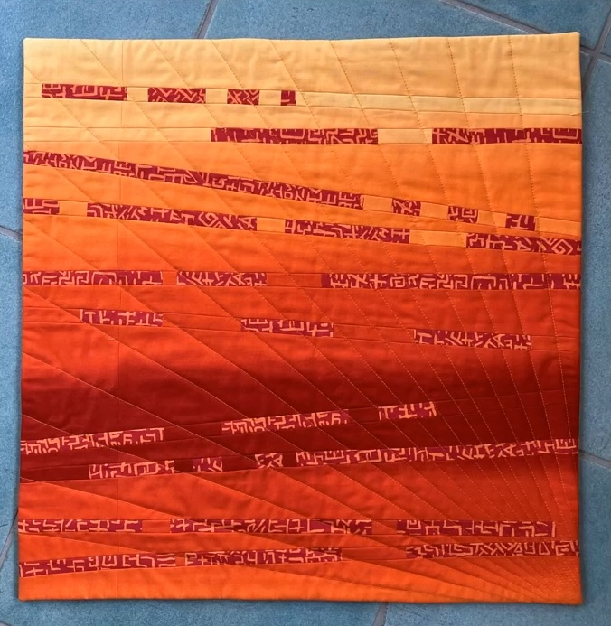 A square quilt with a vibrant orange and red gradient background. The quilt features a repetitive, abstract pattern of small, white lines creating a textured, almost pixelated effect. The lines are arranged in a radial pattern, radiating outwards from the center. The quilt has a red border.