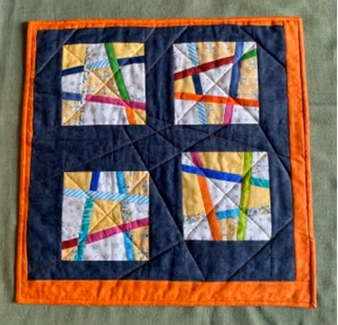 A square quilt with a dark blue background. The quilt is divided into four sections, each featuring a colorful, abstract design with intersecting lines and shapes in various colors. The background is quilted with a linear pattern. The quilt has an orange border.