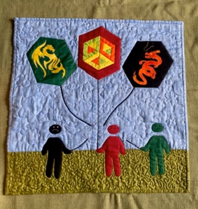 A square quilt with a blue background. The quilt features three colored hexagons, each symbolizing a different zodiac sign: a green dragon, a red dragon, and a yellow scorpion. These hexagons are connected by lines to three figures at the bottom: a black figure, a red figure, and a green figure. The background is quilted with a textured pattern.