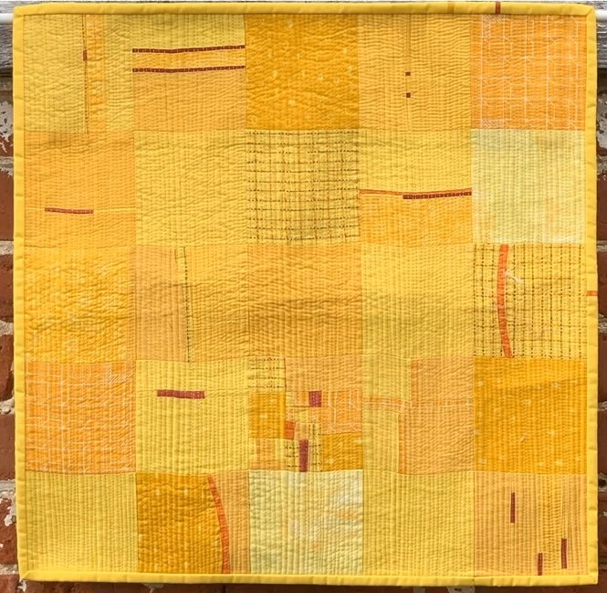 A square quilt with a yellow background. The quilt features a patchwork design with squares in various shades of yellow and orange. Some squares have additional textures or patterns, such as stripes or dots. The background is matchstick quilted. The quilt has a yellow border.
