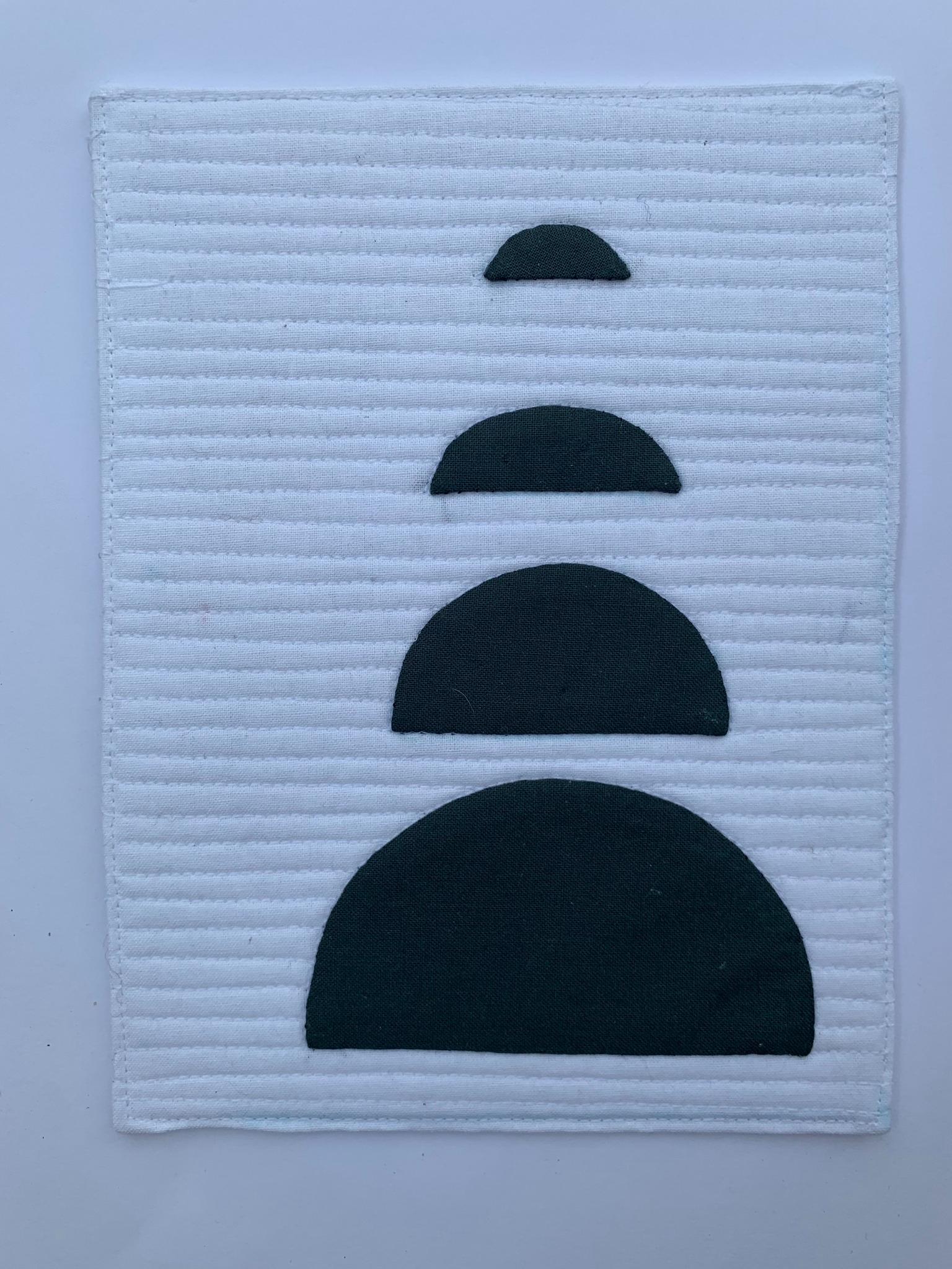 A square quilt with a white background. The quilt features four overlapping black semicircles, arranged in a vertical stack from smallest to largest. The background is quilted with horizontal lines.