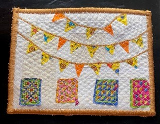 A rectangular quilt with a white background. The quilt features a string of colourful flags hanging from the top and four small, colourful squares at the bottom. The background is quilted with a subtle, linear pattern. The quilt has an orange border.