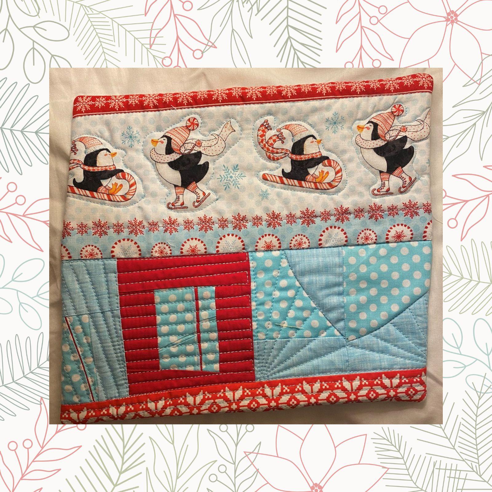A rectangular quilt with a blue background and a red border. The quilt features a row of penguins ice skating across the top, each with a different colored hat. The bottom section is a patchwork of blue and red fabrics with various patterns, including polka dots and snowflakes.