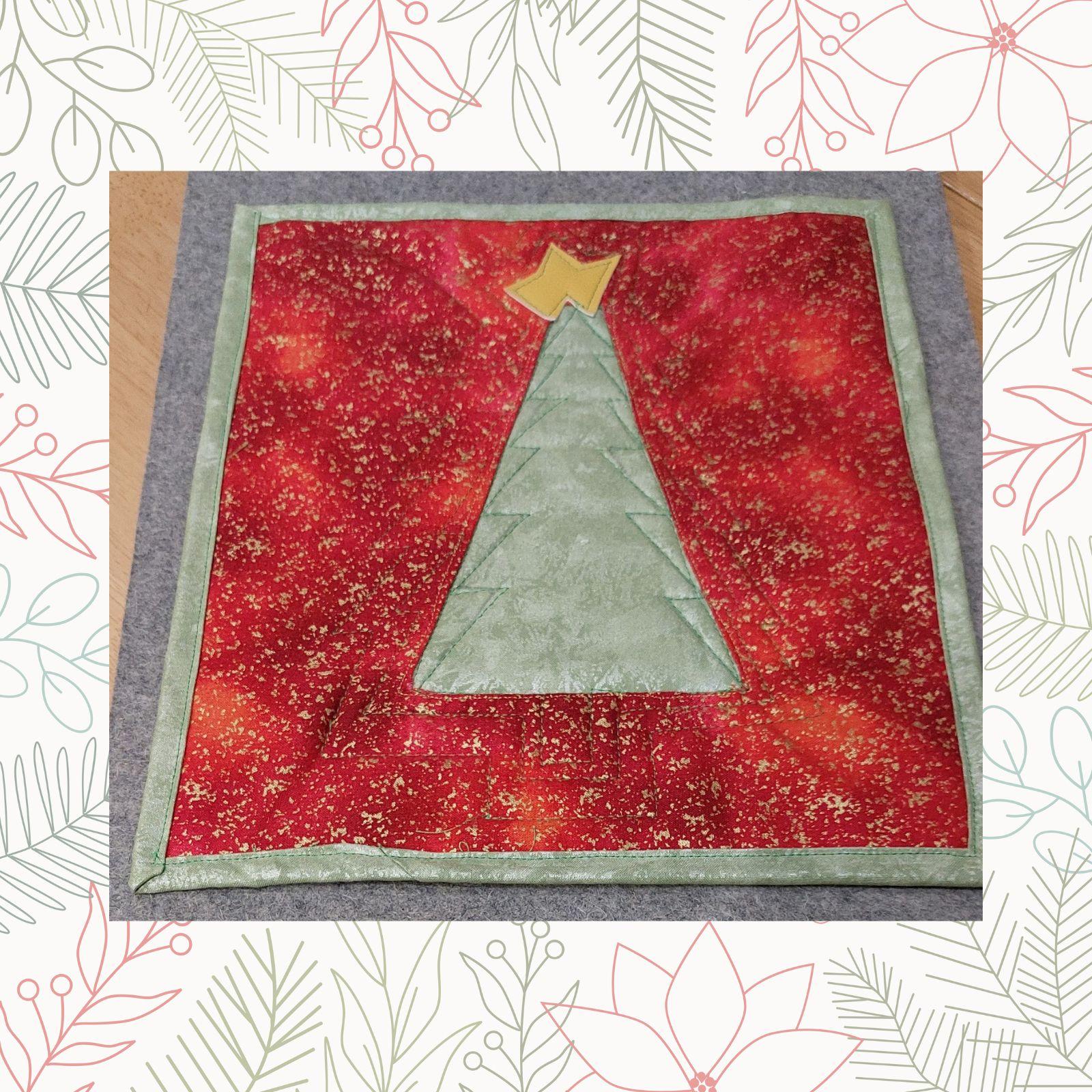 A square quilt with a red background and a green border. The quilt features a green Christmas tree with a yellow star on top. The background has a speckled, textured appearance.