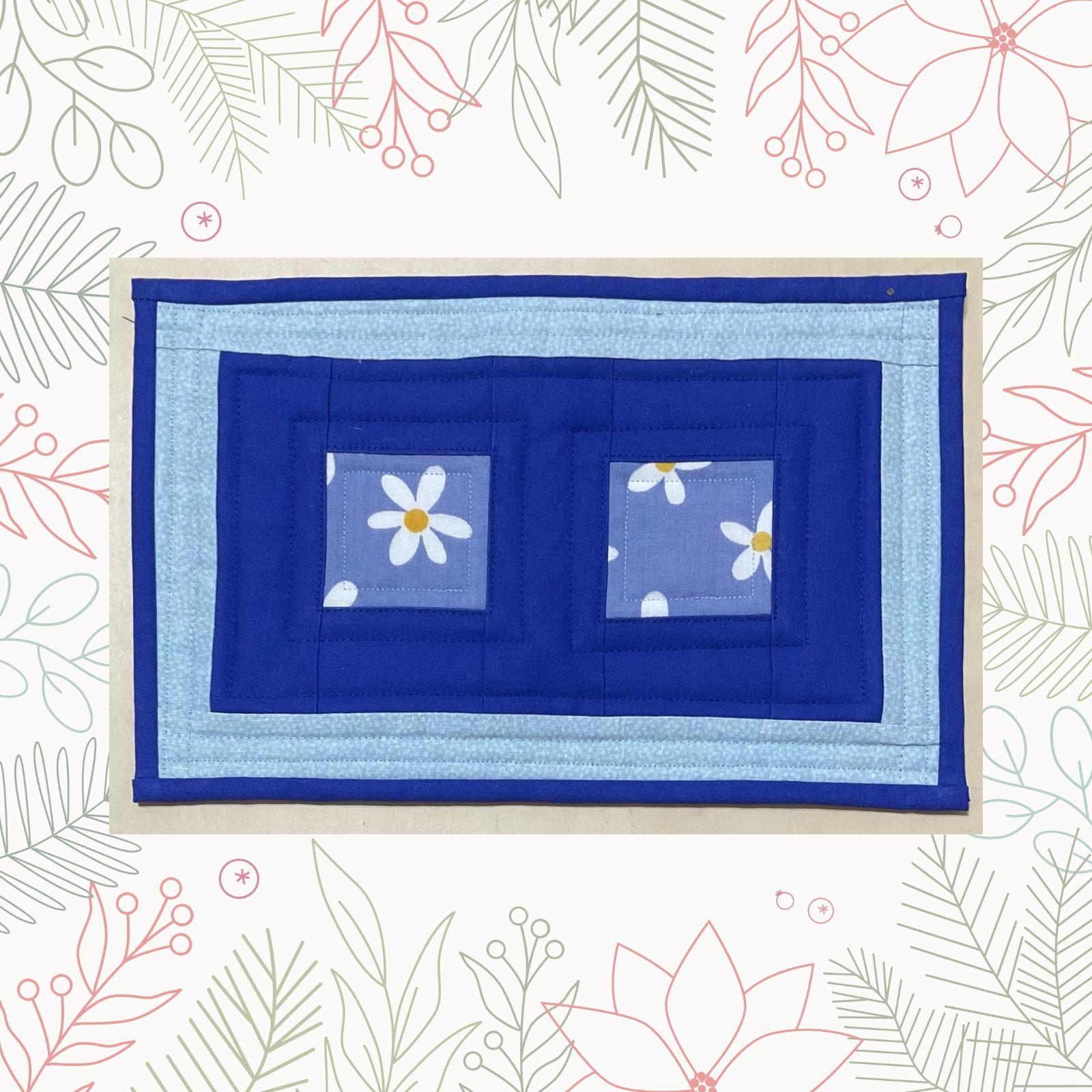 A rectangular quilt with a blue background and a blue border. The quilt features two square windows with a floral pattern inside. The background is quilted echoing the squares.
